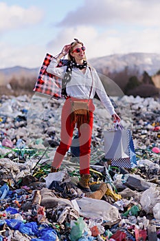 Modern woman on landfill with shopping bags. consumerism versus pollution concept.