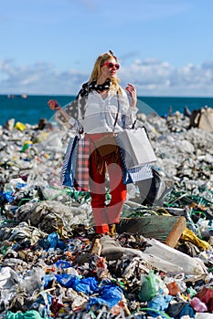 Modern woman on landfill with shopping bags. standing on pile of waste on beach. Consumerism versus pollution concept.
