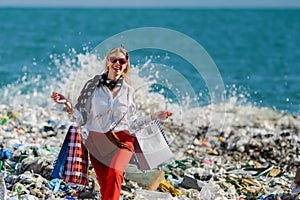 Modern woman on landfill with shopping bags. standing on pile of waste on beach. Consumerism versus pollution concept.