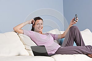 Modern woman relaxed on couch with phone, laptop