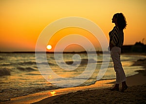 Modern woman on seacoast in evening looking into distance