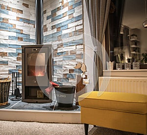 Modern wood fired stove burning with fire-wood. Kindling bucket, wicker log basket and briquettes in front of brick wall. Yellow