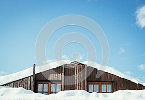 Modern wood house with windows and snow on the roof, blue sky with text space