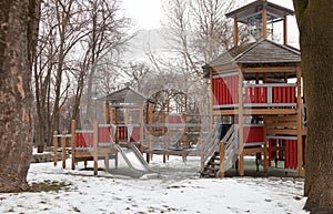 Modern wooden playground for young children during winter season. Natural frame with trees