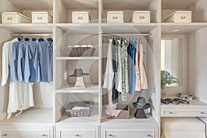 Modern wooden wardrobe with clothes hanging on rail in walk in c