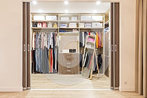 Modern wooden wardrobe with clothes hanging on rail in walk in closet