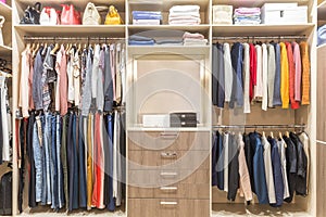 Modern wooden wardrobe with clothes hanging on rail in walk in closet