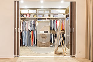 Modern wooden wardrobe with clothes hanging on rail in walk in closet