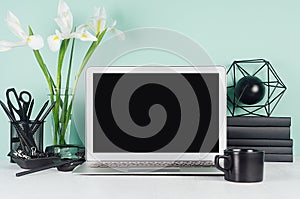 Modern workplace with blank computer display, black stationery, books, coffee cup, abstract atom model, white  bouquet in green.
