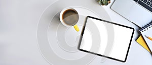 Modern workplace with digital tablet, laptop and coffee cup on white table.