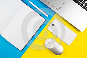 Modern workplace with notebook, computer mouse, mobile phone and white pen on blue and yellow color background