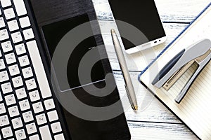 Modern workplace with laptop, silver pen, smartphone, notepad and stapler on white wooden vintage table