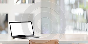 Modern workplace with open blank screen laptop computer on empty white wooden desk with blurred office