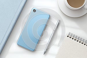 Modern workspace with blue smartphone, silver pen, notebook, book and coffee cup on white desk in natural light