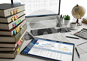 Modern workspace featuring a stack of books, tablet with calendar, keyboard, globe, and coffee mug on a white desk