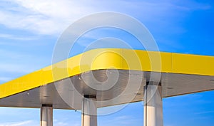 Modern yellow canopy roof of outdoor distribution service point with columns of gas station against blue sky background