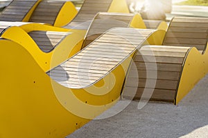 Modern yellow curved wooden benches for relaxing in city park on sunny day. Public city resting area design