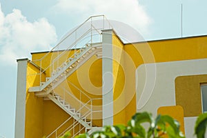 Modern yellow and white house with metal zigzag staircase. Courtyard of a building, beautification