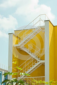 Modern yellow and white house with metal zigzag staircase. Courtyard of a building, beautification