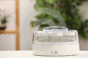 Modern yogurt maker with empty jars on white table indoors. Space for text