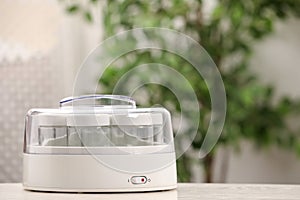 Modern yogurt maker with empty jars on white table indoors. Space for text