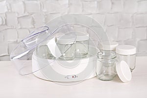 Modern yogurt maker with empty jars on white wooden table