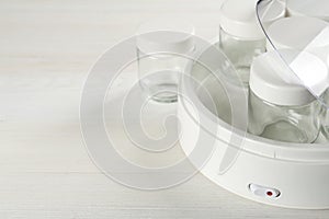 Modern yogurt maker with empty jars on white wooden table, closeup. Space for text