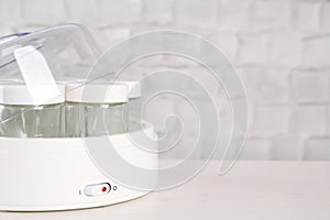 Modern yogurt maker with empty jars on white wooden table, closeup. Space for text