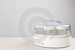 Modern yogurt maker with empty jars on white wooden table, space for text