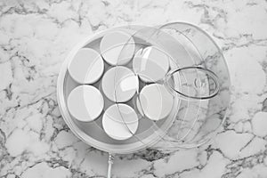 Modern yogurt maker with jars on white marble table, top view