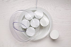 Modern yogurt maker with jars on white wooden table, flat lay