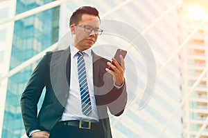 Modern young businessman wear black suit hand holding smartphone. Professional business man standing outside office