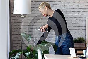 Modern young entrepreneur woman watering plants in the office