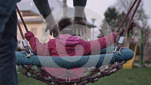 Modern young father swinging his 5-year-old daughter, little girl, on a childrens swing in the middle of a kids playground