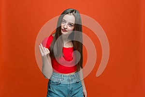 Modern young girl doing money gesture with hands, asking for salary payment, donation, debt on orange studio background