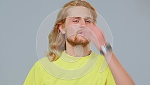 Modern young guy with long blond hairs removes elastic band from hair, walking, preening. Haircare cosmetics advertising