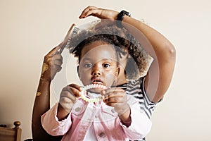 Modern young happy african-american family: mother combing daughters hair at home, lifestyle people concept