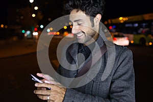 Modern young man using his mobile phone in the street at night.