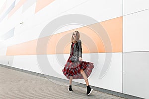 Modern young woman in sunglasses in fashionable black-red clothes and shoes is dancing in street near modern building. Urban