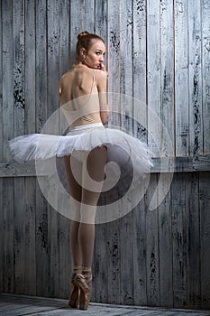 Modest ballerina standing near a wooden wall