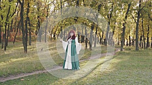 Modest cute lady with red curled hair, large plump model in green loose national dress holding apple in her hands