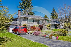 Modest residential house with red car parked on driveway in front. Family house with blossoming flowers on the yard