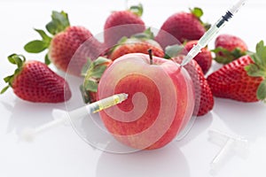 Modified food, apple and strawberries with punched needles and syringes / isolated on a white background