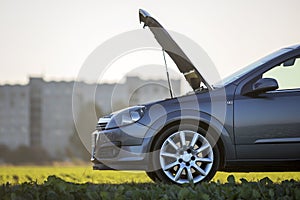 Modified image of a fictional non existent car. Car with open hood on empty gravel field road on blurred bright sky copy space