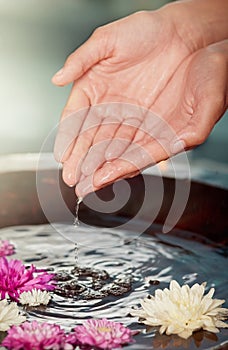 Moisture is the essence of healthy skin. a womans hands in a flower filled water bowl at a spa.