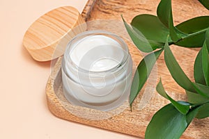 Moisturizer cream jar in matte glass bottle and green leaves on beige background. Cosmetics for skin and body care