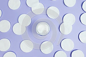 Moisturizer cream in open glass jar, cotton pads on light purple background. Top view. Natural bio organic eco skincare beauty