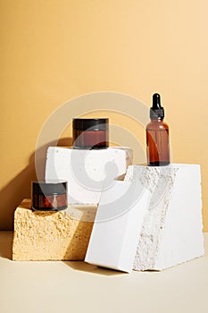 Moisturizers creams jars, serum in glass bottle and white box on beige background. Open jar and bottle. Copy space. Set for