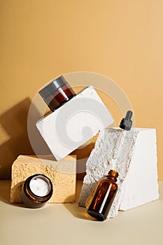 Moisturizers creams jars, serum in glass bottle and white box on beige background. Open jar and bottle. Copy space. Set for