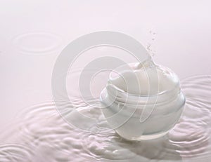 Moisturizing cosmetic cream on the pink milk background with milk splash and drops